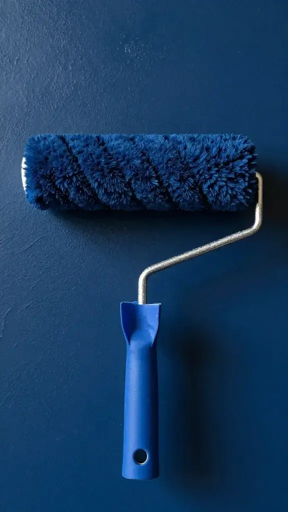 Closeup of paint roller with navy blue paint on wall